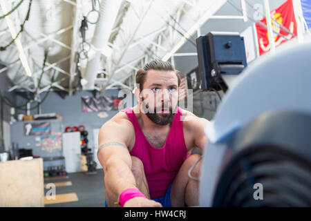 Mixed Race man using rowing machine in gymnasium Stock Photo