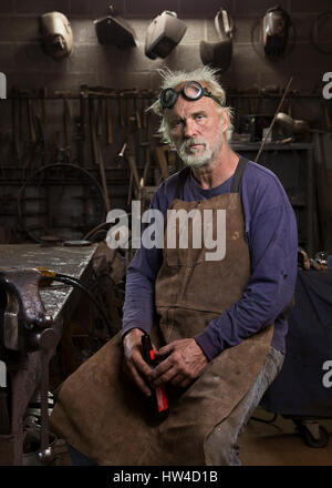 Portrait of serious Caucasian blacksmith in workshop drinking beer Stock Photo