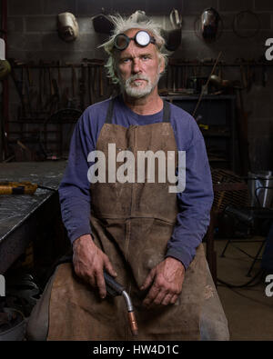 Portrait of serious Caucasian blacksmith in workshop holding torch Stock Photo