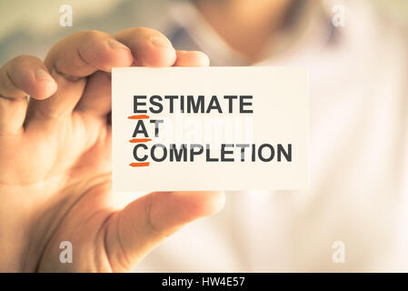 Closeup on businessman holding card with EAC ESTIMATE AT COMPLETION acronym text, business concept image with soft focus background and vintage tone Stock Photo
