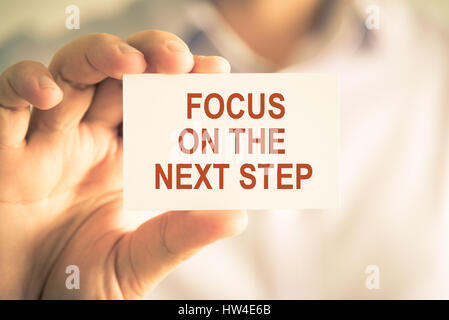 Closeup on businessman holding a card with text FOCUS ON THE NEXT STEP, business concept image with soft focus background and vintage tone Stock Photo