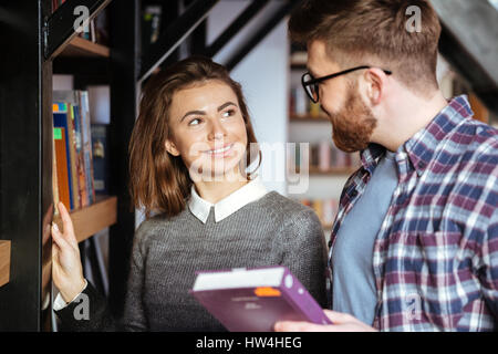 Two students communicating in library standing at the bookshelf Stock Photo
