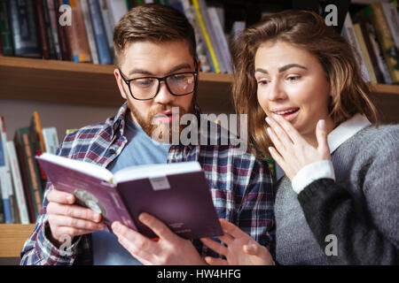 Two smart students reading and studying in library while searching through books on the shelves Stock Photo
