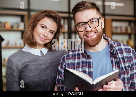 Happy man and woman students preparing for exams in library together and looking at camera Stock Photo