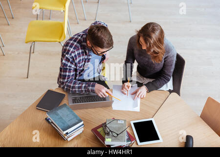 Image of young concentrated students sitting in library while writing notes. Stock Photo