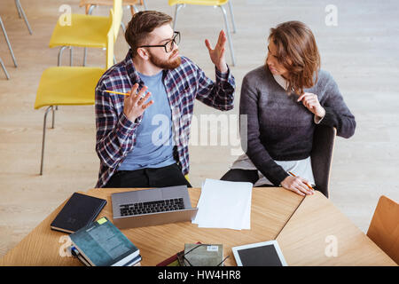 Picture of angry students sitting in library while writing notes and quarrel. Stock Photo