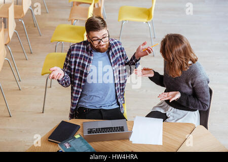 Top view of cheerful young students man and woman discussing project while sitting at the table in library Stock Photo