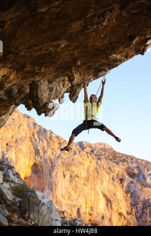 Male rock climber trying to reach handhold, about to fall off cliff, climbing challenging route on ceiling of cave Stock Photo
