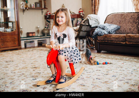 girl on a toy horse at home Stock Photo