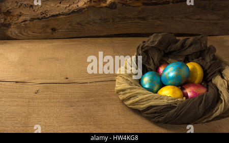 Multi-colored Easter eggs in a nest of soft scarf on a natural wooden background. Copy space. Stock Photo