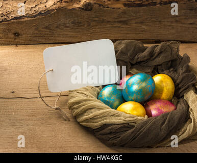 Multi-colored Easter eggs in a nest of soft scarf on a natural wooden background. Copy space. Stock Photo