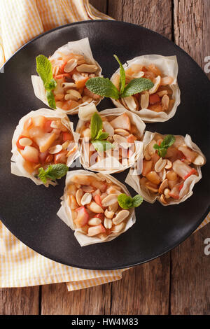 Cups of dough filo stuffed with apples and peanuts close-up on a plate. Vertical view from above Stock Photo