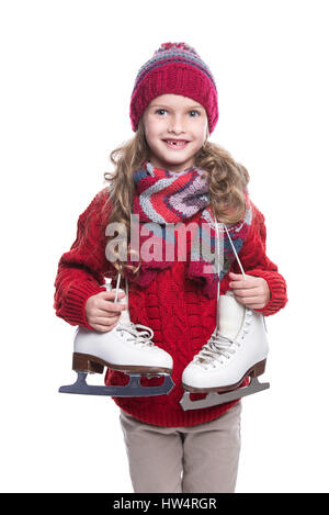 Cute smiling little girl with curly hairstyle wearing knitted sweater, scarf, hat and gloves with skates isolated on white background. Winter clothes  Stock Photo