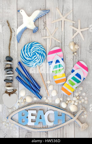 Abstract beach art collage with flip flops, candy rock, seashells, pearls and decorative seaside items on distressed white wood forming a background. Stock Photo