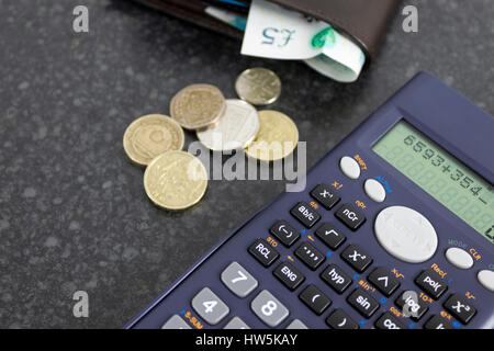 Scientific calculator on a black desk with a wallet showing a five pound note and some loose change Stock Photo
