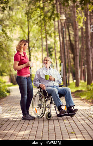 Smiling young woman with her disabled father in wheelchair enjoying time together outdoor Stock Photo