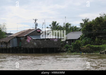 A shanty town at riverside of dirty river Mekong in Vietnam. Wooden cottages are set on a wooden pillars, fixed into muddy river bed. Stock Photo