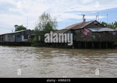 A shanty town at riverside of dirty river Mekong in Vietnam. Wooden cottages are set on a wooden pillars, fixed into muddy river bed. Stock Photo