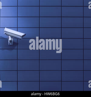 Horizontal front view of a surveillance monitoring white camera viewed from a side with blue background wall of metallic plates, copyspace on the righ Stock Photo