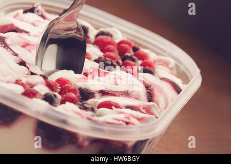 horizontal close up of chrome teaspoon stuck in vanilla ice cream with mix of black and red frozen berries on brown background selective focus Stock Photo