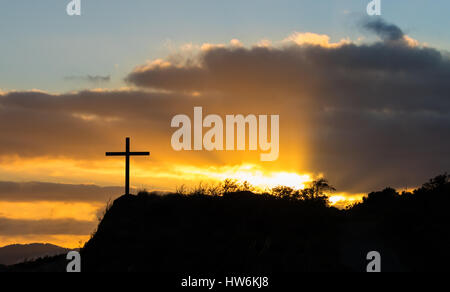 The light of early morning sun breaking through grey clouds behind a black cross. Stock Photo