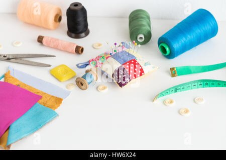 Sewing tools including fabric, scissors, needles , spools of different color thread, measure tape, buttons on a white background with a empty space for the text. Sewing tools fashion design. Stock Photo