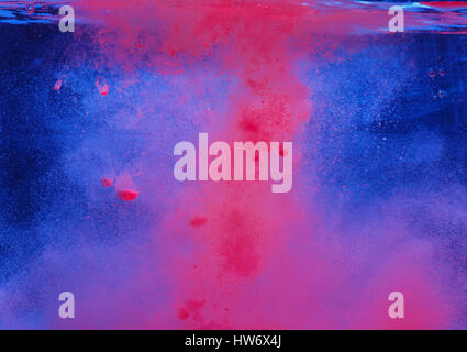 Abstract image of a pink powder falling into a blue liquid Stock Photo