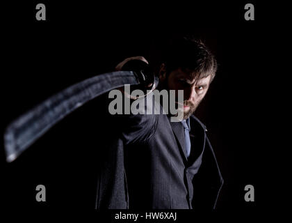 stern angry businessman in a wool coat with sword in dark background Stock Photo