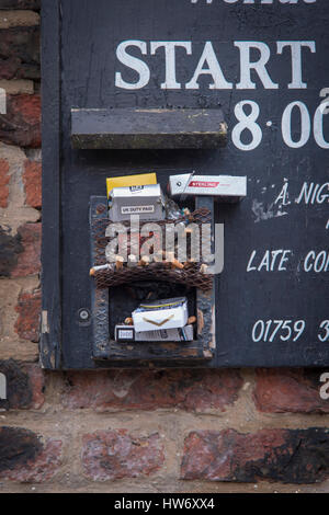 Close-up of used cigarette butts and empty packets discarded in a wire holder attached to a pub sign - York, North Yorkshire, England, UK. Stock Photo