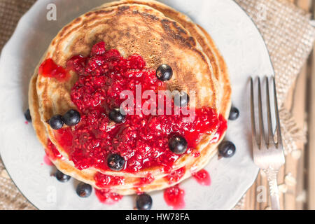 Delicious Oatmeal Pancake with raspberry jam and decorated with black currant. Top view, flat lay. Shallow DOF Stock Photo