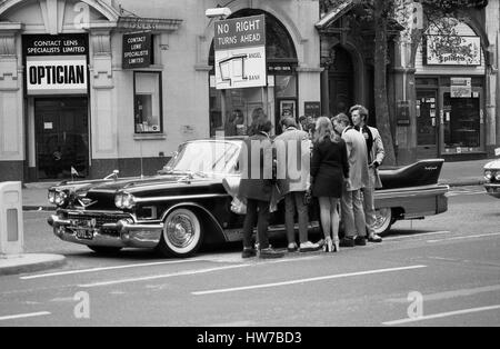 Music fans admire a vintage U.S. car during the Rock and Roll Radio Campaign march through Central London, England on May 15, 1976. The campaign aimed to get more vintage rock and roll music played on BBC radio. Stock Photo