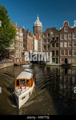 AMSTERDAM, NETHERLANDS- SEPTEMBER 27, 2016: Boats cruising the canal with the Church of St. Nicholas tower in the distance. Stock Photo