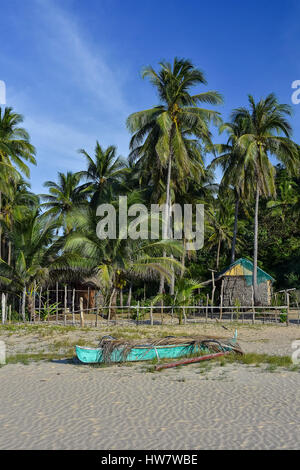 A basic Filipino pump boat on the shore of a white sand beach with a back ground of fenced area, palm trees and a basic bamboo hut. Stock Photo