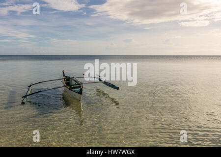 A Filipino fisherman's basic pump boat floating empty on a still calm tropical sea with seagulls resting on its stabilisers. Stock Photo