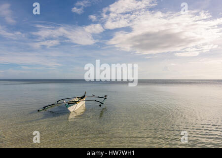 A Filipino fisherman's basic pump boat floating empty on a still calm tropical sea with seagulls resting on its stabilisers. Stock Photo