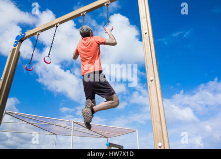 Mature man performing pull ups on rings in park Stock Photo