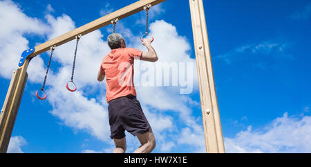 Mature man performing pull ups on rings in park Stock Photo