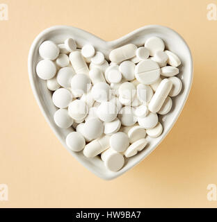 heart shaped bowl of white pills on beige paper background, top view Stock Photo