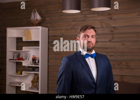 Portrait of serious groom in suit and bow tie, wooden room interior on background Stock Photo