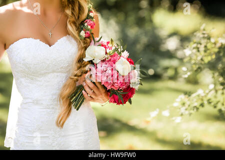 Bride holding delicate marriage bouquet. Beautiful sunny day in park. Stock Photo