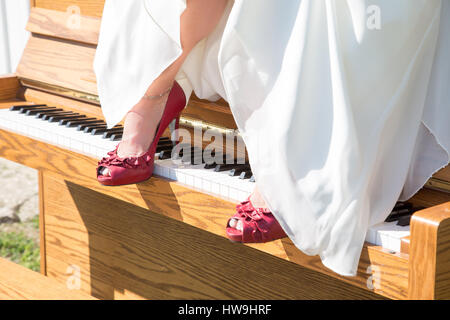 A brides red shoes rest on the keys of a piano that sits outside in the sun Stock Photo