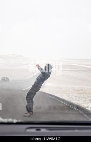 Woman tries to stand against snow flurry seen through a windshield. Stock Photo
