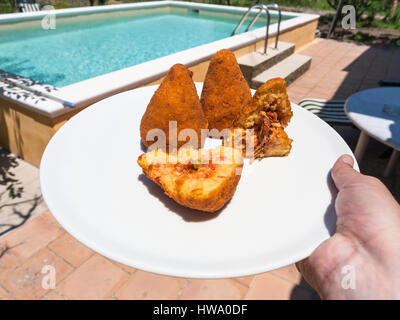 travel to Italy, italian cuisine - traditional arancini ( fried rice filled balls with filling coated with breadcrumbs) on rural backyard in Sicily Stock Photo