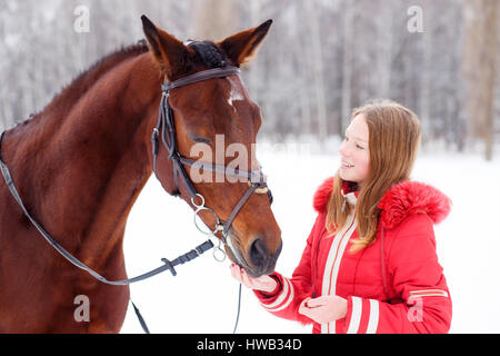 Teenage girl feeding bay horse on winter field. Friendship concept image Stock Photo