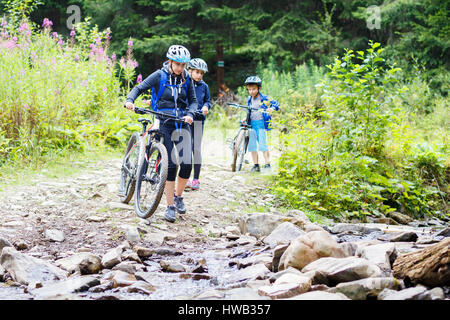 Young woman with her children on bikes wade the mountain creek Stock Photo