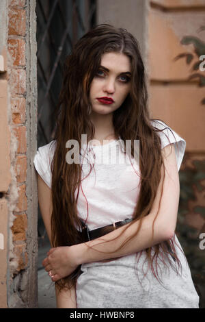 Beautiful serious girl with blank look, red lips in white t-shirt standing in old park. Picture of giythic halloween girl. Fashion shot of serious gir Stock Photo