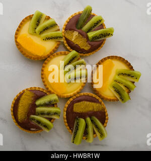 round vanilla and chocolate tarts with kiwi and orange on table Stock Photo