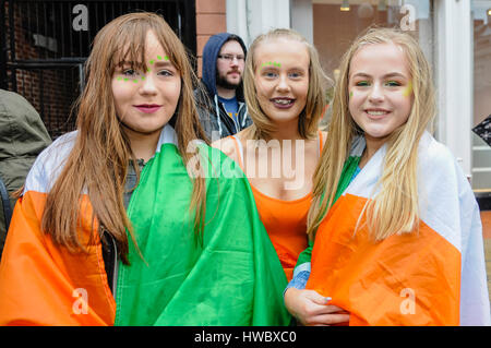 Belfast, Northern Ireland. 17 Mar 2016 - Three young girls wear Irish Tricolours over their shoulders as they stant in the crowd to celebrate Saint Patrick's Day. Stock Photo