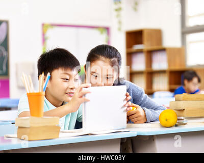 asian elementary schoolgirl and school boy using tablet computer together in classroom. Stock Photo