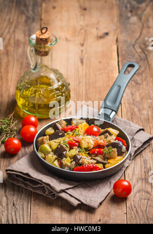 Vegetable ratatouille: steamed zucchini, eggplant, tomatoes, bell peppers, onion, garlic, thyme in a frying pan on wooden background Stock Photo